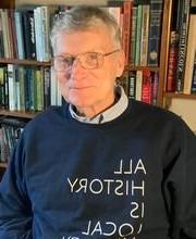Dr. William Hanna wearing dark blue sweatshirt that says "All History is Local" in front of a bookcase