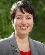 headshot photo of Dr. Sarah Wiggins smiling with short dark brown hair wearing a red blouse under a gray blazer with a sun pin on the lapel