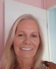 Nancy Monroe smiling with long gray/blonde hair in front of a white door on a pink wall