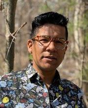 headshot photo of Dr. Luis Paredes with short wavy dark hair, wearing light brown glasses and a floral button down shirt with a dark background. Woods are 