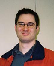 Dr. Michael Zimmerman smiling with short dark brown hair and glasses wearing an orange parka with black collar over a navy blue button down shirt