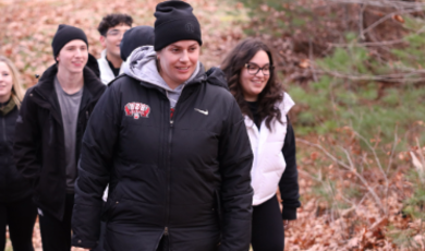 一个戴黑帽子穿黑夹克的女人领着一群人走在树林里的小路上 