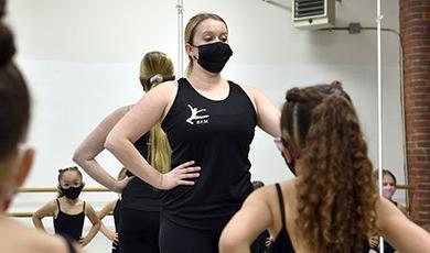 Riley Lathrop teaches dance to young students with a large mirror behind her.